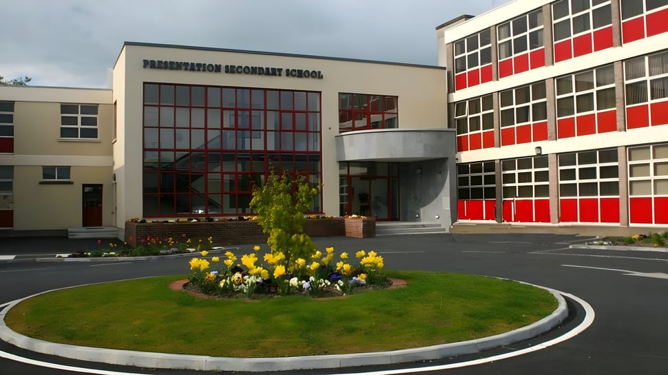 Das moderne Hauptgebäude der Presentation Secondary School Thurles mit großen Fenstern und einem kreisförmigen Blumenbeet im Vordergrund.
