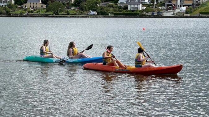Schüler der Presentation Secondary School in Cork paddeln mit bunten Schwimmwesten auf aufblasbaren Kajaks auf ruhigem Wasser.