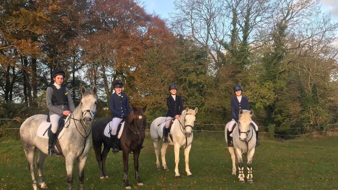 Eine Gruppe von Schülerinnen und Schülern der Presentation Secondary School in Tipperary reitet auf Pferden auf einer Wiese mit herbstlichem Baumbestand.