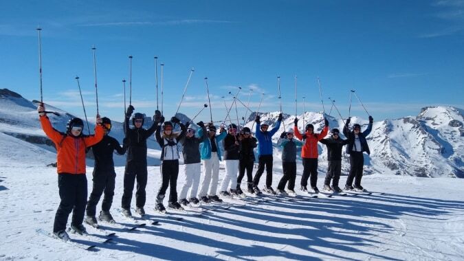 Eine Gruppe von Schülerinnen und Schülern der Presentation Secondary School (Thurles) steht in Winterkleidung auf einem verschneiten Berghang mit schneebedeckten Gipfeln im Hintergrund.