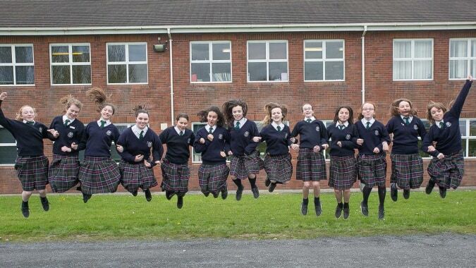 Eine Gruppe von Schülerinnen in Schuluniform steht vor einem Backsteingebäude auf dem Campus der Presentation Secondary School Kilkenny.