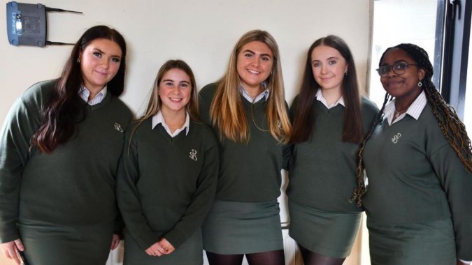 Fünf Schuelerinnen in Schuluniform stehen gemeinsam und lächeln im Flur der Presentation Secondary School in Cork.