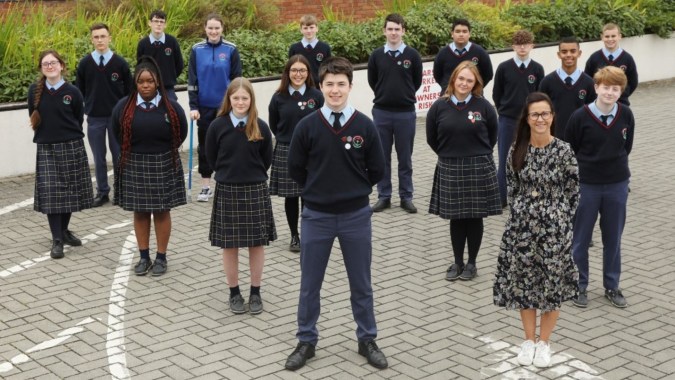Eine Gruppe von Schülerinnen und Schülern in Schuluniformen steht auf dem gepflasterten Außenbereich des Presentation College Carlow.
