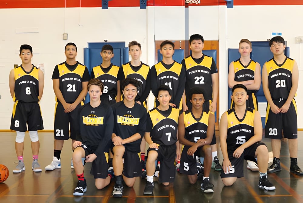 Eine Gruppe junger Basketballspielerinnen in gelb-schwarzen Trikots posiert in der Turnhalle der Prince of Wales Secondary School.