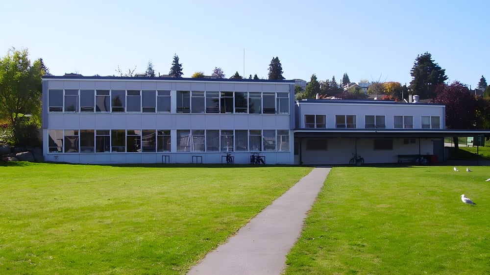 Das moderne Glasgebäude der Prince of Wales Secondary School steht auf einem grasbewachsenen Feld unter blauem Himmel.