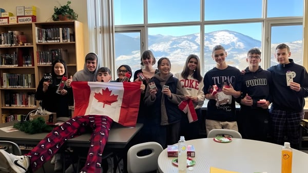 Eine Gruppe von Schülerinnen und Schülern der Princess Margaret Secondary School hält eine kanadische Flagge in einem Aufenthaltsraum mit Blick auf verschneite Berge.
