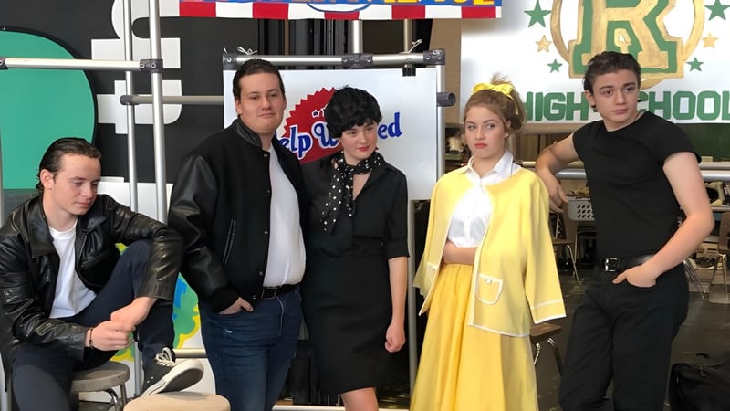 Eine Gruppe von Schülerinnen und Schülern der Princess Margaret Secondary School steht in einem Aufnahme- und Probenraum mit bunten Fahnen im Hintergrund.