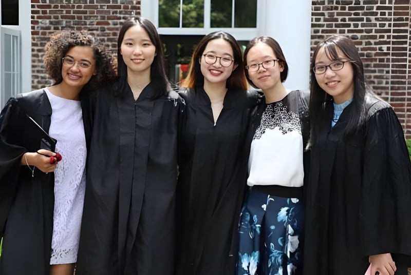 Fünf Schülerinnen in Abschlussroben stehen vor einem Backsteingebäude auf dem Campus der Princeton International School of Mathematics & Science.