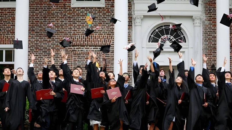 Absolventinnen und Absolventen der Princeton International School of Mathematics & Science werfen ihre Abschlussmützen vor einem Backsteingebäude in die Luft.