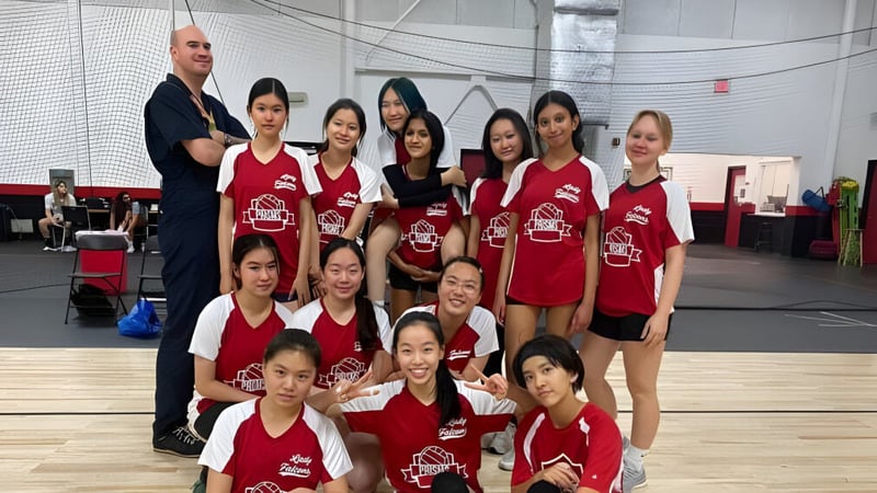 Eine Gruppe junger Schülerinnen in roten Uniformen posiert in einer Sporthalle der Princeton International School of Mathematics & Science mit einem Mann im Hintergrund.