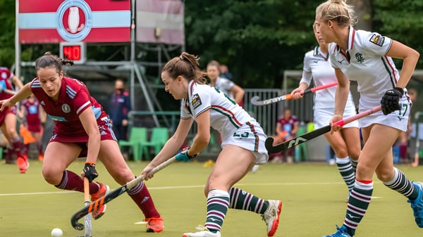 Schülerinnen der Prior’s Field School spielen ein Feldhockeyspiel auf dem Sportplatz mit Zuschauertribünen im Hintergrund.