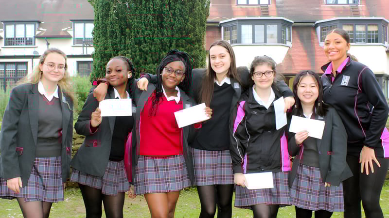 Schülerinnen von Prior's Field stehen vor einem mit Efeu bedeckten Gebäude und halten Urkunden in der Hand.