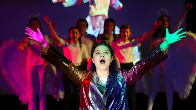 Eine junge Frau mit erhobenen Armen tanzt bei einer Veranstaltung auf dem Campus der Prior's Field School umgeben von bunt gekleideten Schülern.