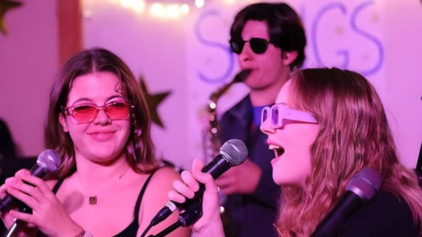 Drei Personen der Proctor Academy treten mit Mikrofonen auf einer farbenfrohen Bühne auf.