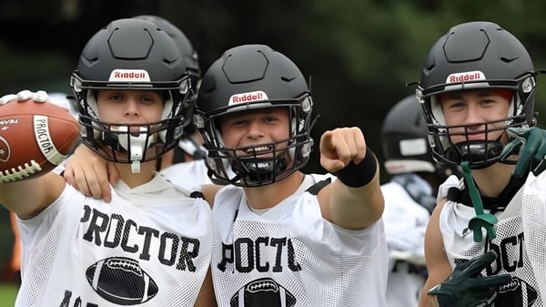 Drei Schüler der Proctor Academy in Football-Uniformen stehen zusammen und halten einen Football auf einem Sportfeld.