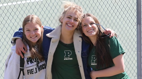 Drei Schülerinnen der Proctor Academy umarmen sich lachend vor einem Drahtzaun.