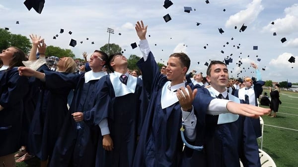 Absolventen der Prospect High School werfen ihre blauen Abschlussmützen auf dem Sportplatz in die Luft.