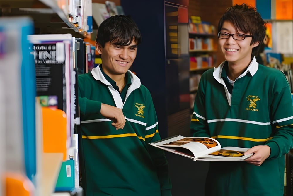 Zwei Schülerinnen der Prospect High School stehen in der Bibliothek, eine von ihnen hält ein offenes Buch.