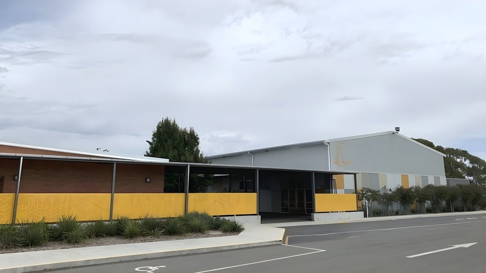 Das einstöckige Gebäude der Prospect High School mit gelber Fassade und überdachtem Eingang ist von einem Parkplatz und Bäumen umgeben.
