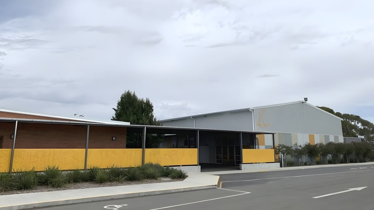 Das einstöckige Gebäude der Prospect High School mit gelber Fassade und überdachtem Eingang ist von einem Parkplatz und Bäumen umgeben.