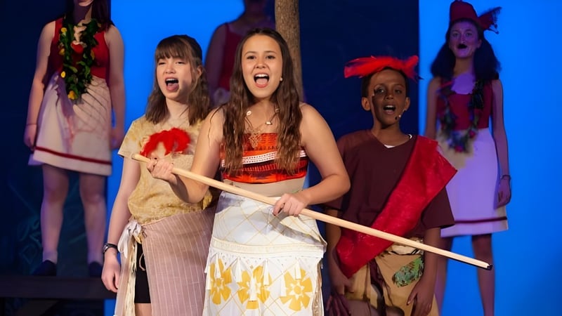 Eine Gruppe Schülerinnen der Providence Christian Academy führt auf der Bühne vor einem blauen Hintergrund mit bunten Kostümen auf.