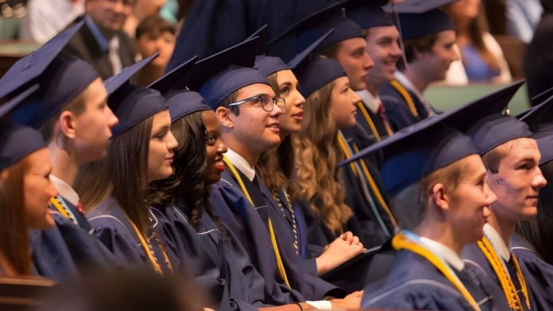 Eine Gruppe von Absolventinnen und Absolventen der Providence Christian Academy steht bei einer feierlichen Zeremonie in akademischer Kleidung zusammen.