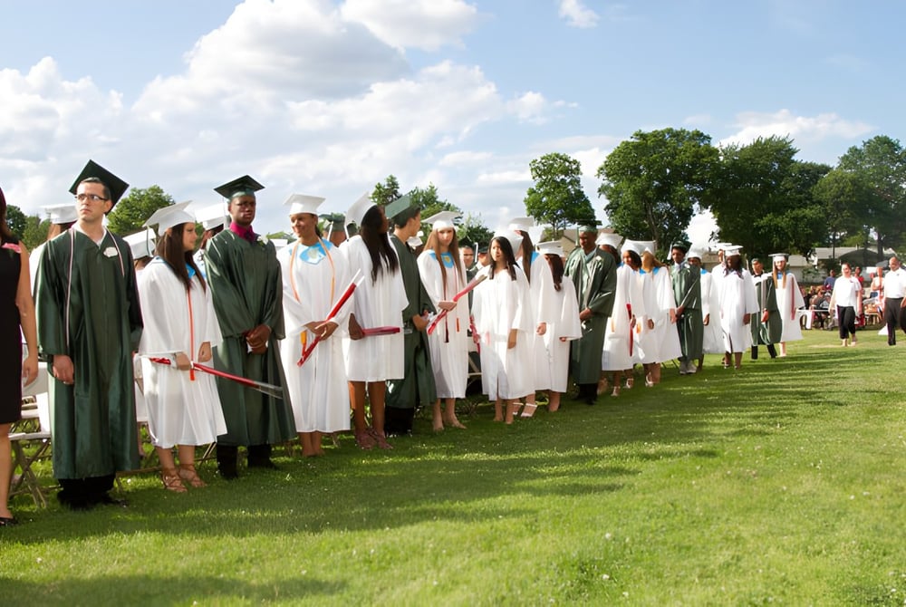 Eine Gruppe von Absolventinnen und Absolventen des Provo City School District steht auf einer Wiese mit Bäumen und bewölktem Himmel im Hintergrund.