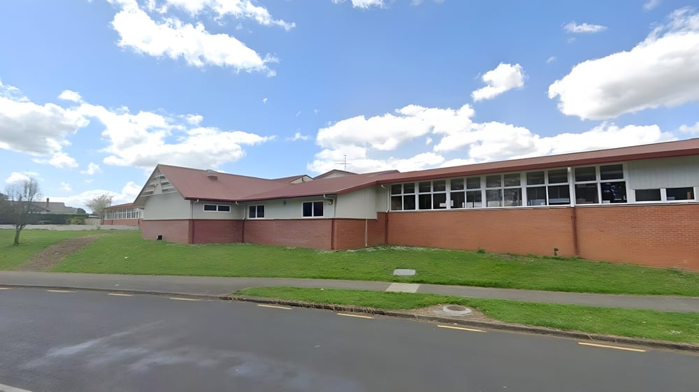 Das Backsteingebäude mit rotem Dach steht auf dem Gelände der Pukehohe High School, umgeben von Gras und einer befestigten Straße.