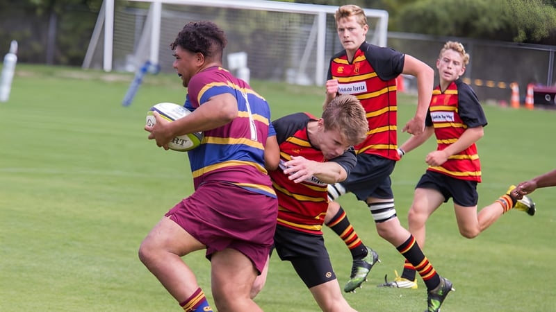 Schüler der Pukehohe High School spielen Rugby auf einem Sportfeld und führen einen Tackle während des Spiels aus.