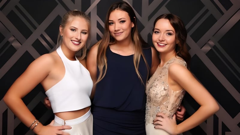 Drei Schülerinnen der Pukehohe High School posieren gemeinsam vor einem dunklen, geometrischen Hintergrund.