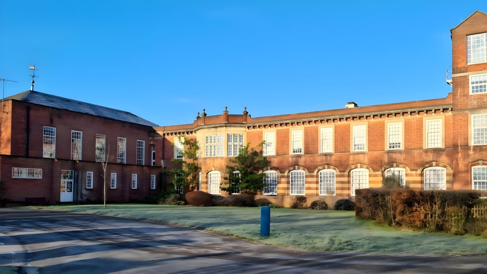 Das Backsteingebäude der The Purcell School for Young Musicians ist von einer Grünfläche mit Fußgängerüberweg umgeben.