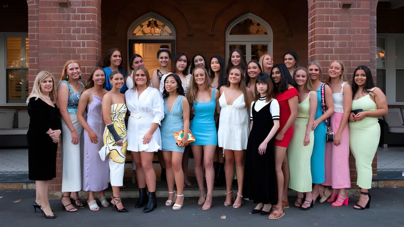 Eine Gruppe von Schülerinnen des Pymble Ladies College steht vor einem Backsteingebäude mit Rundbogenfenstern.