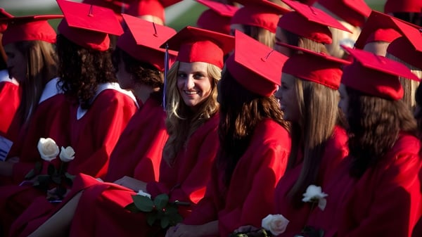 Eine Gruppe von Absolventinnen und Absolventen der Quad Cities Christian School steht in roten Talaren mit Blumen vor grünem Hintergrund.