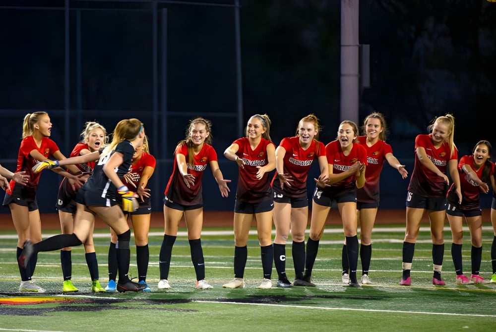 Eine Gruppe junger Athletinnen der Quad Cities Christian School steht in roten Trikots auf einem Sportfeld bei Nacht.