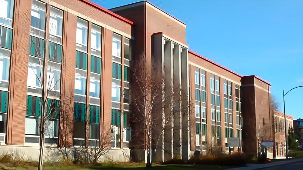 Das mehrstöckige Backsteingebäude der Québec High School mit großen Fenstern und einem markanten Eingang vor klarem blauen Himmel.