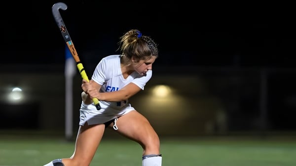 Eine Sportlerin der Queen Anne’s School hält ein Hockeyschläger auf einem nachts beleuchteten Spielfeld.