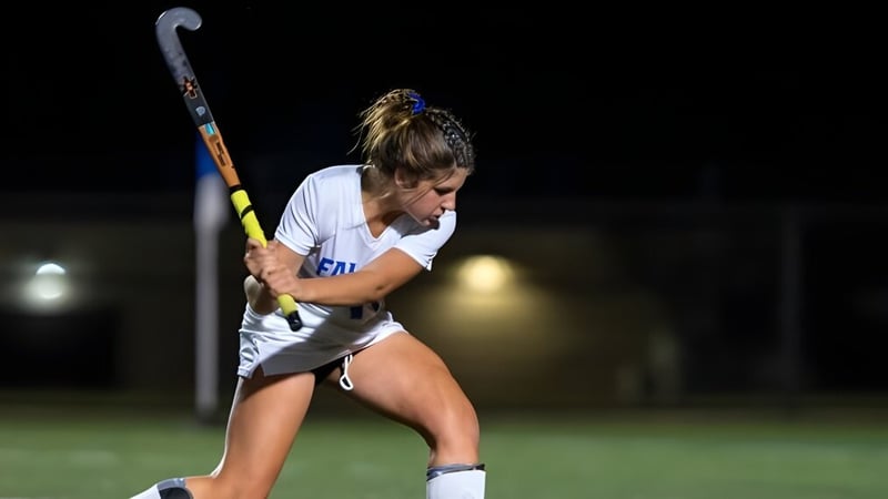 Eine Sportlerin der Queen Anne’s School hält ein Hockeyschläger auf einem nachts beleuchteten Spielfeld.