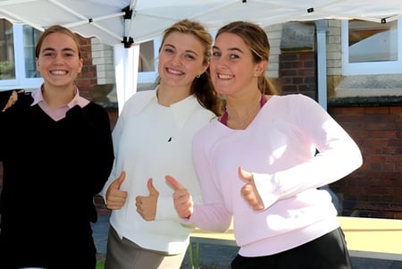 Drei lächelnde Schülerinnen stehen vor einem Gebäude auf dem Campus der Queen Anne’s School.