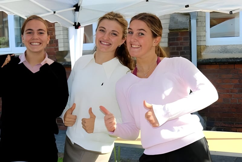 Drei lächelnde Schülerinnen stehen vor einem Gebäude auf dem Campus der Queen Anne’s School.