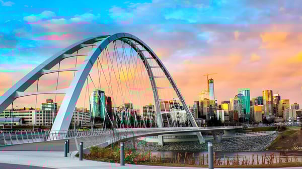 Ein modernes Bogenbrücke überquert einen Fluss mit einem Stadtpanorama hinter dem Campus der Queen Elizabeth High School bei Sonnenuntergang.