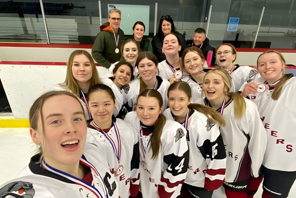 Eine Gruppe von Schülerinnen der Queen Elizabeth Regional High posiert in Hockey-Uniformen auf einer Eisbahn.
