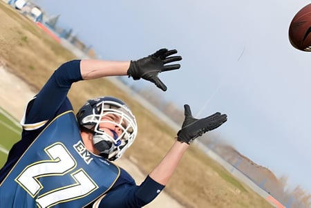 Ein Footballspieler in dunkelblauer Uniform fängt einen Football auf dem Sportplatz der Queen Elizabeth School.