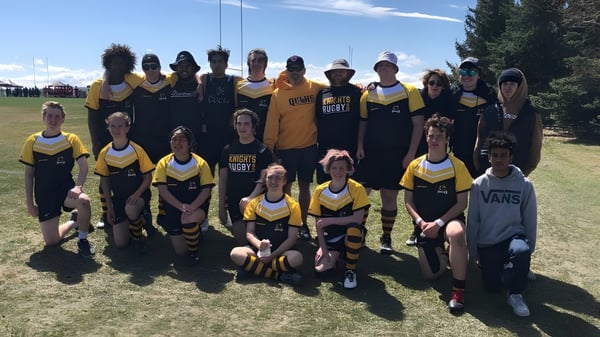 Eine Gruppe von Schülerinnen und Schülern der Queen Elizabeth School posiert auf einem Rasenfeld mit Bergen im Hintergrund.