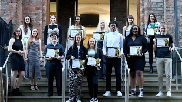 Schüler der Queen Elizabeth’s 6th Form stehen mit Zertifikaten vor einem Backsteingebäude.