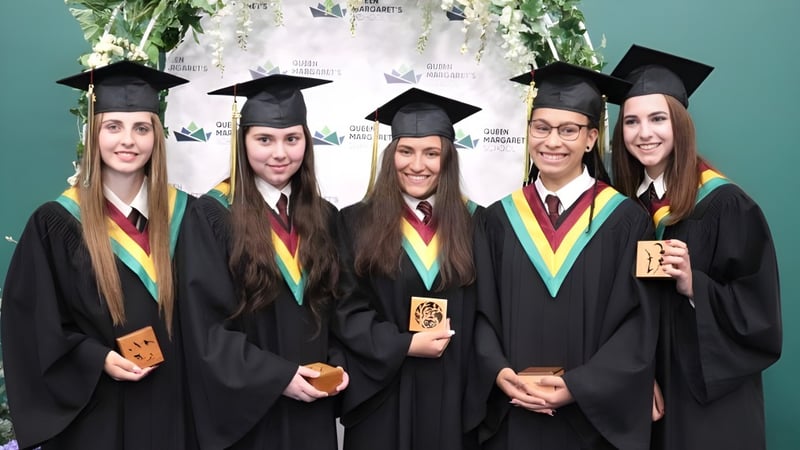 Fünf Schüler der Queen Margaret’s School stehen in ihren Abschlusskutten und halten ihre Diplome vor einem Universitätslogo.