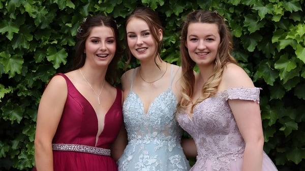 Drei Schülerinnen der Queen Margaret's School for Girls posieren zusammen vor grünem Blattwerk.