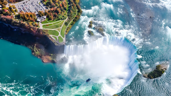 Ein Wasserfall fließt über einen Felsen vor einem See mit herbstlichem Laub auf dem Gelände von Queen Margaret’s School.