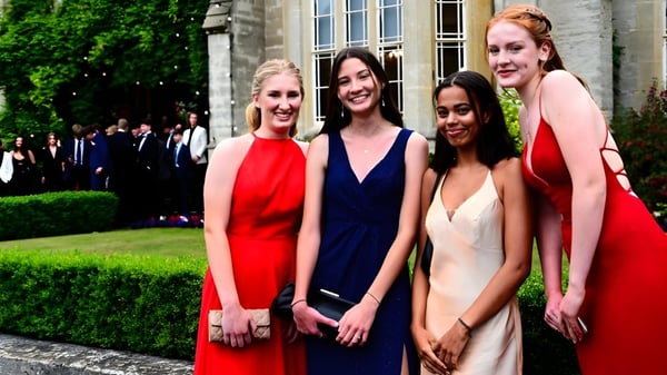Vier junge Frauen in formaler Kleidung stehen in einem Garten auf dem Gelände des Queen’s College.