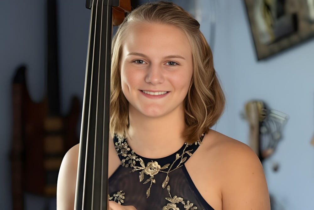 Eine Schülerin der Queensbury High School hält ein Cello in einem Raum mit Kunstwerken an den Wänden.