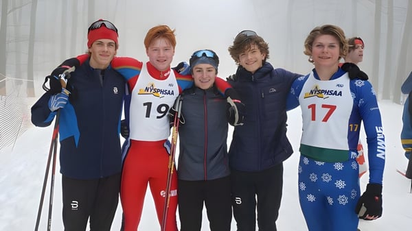 Eine Gruppe Schüler der Queensbury High School steht in Wintersportkleidung in einer verschneiten Waldlandschaft.